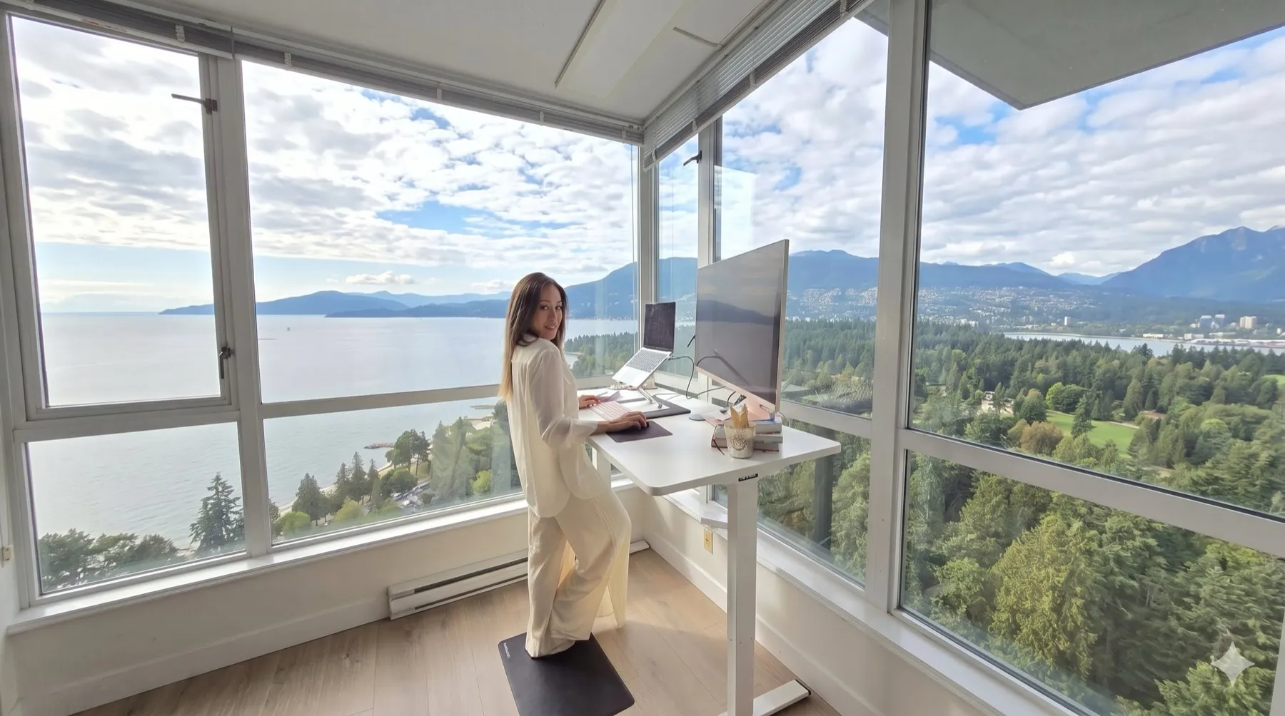 Katy working at a standing desk in a glass corner office overlooking the mountains and sea